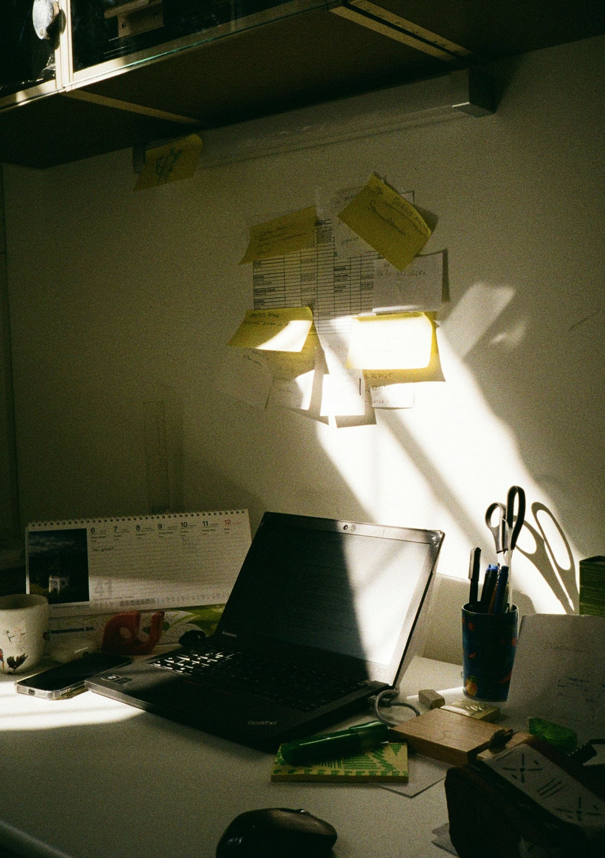 Schreibtisch im Sonnenlicht mit Notizzetteln an der Wand.