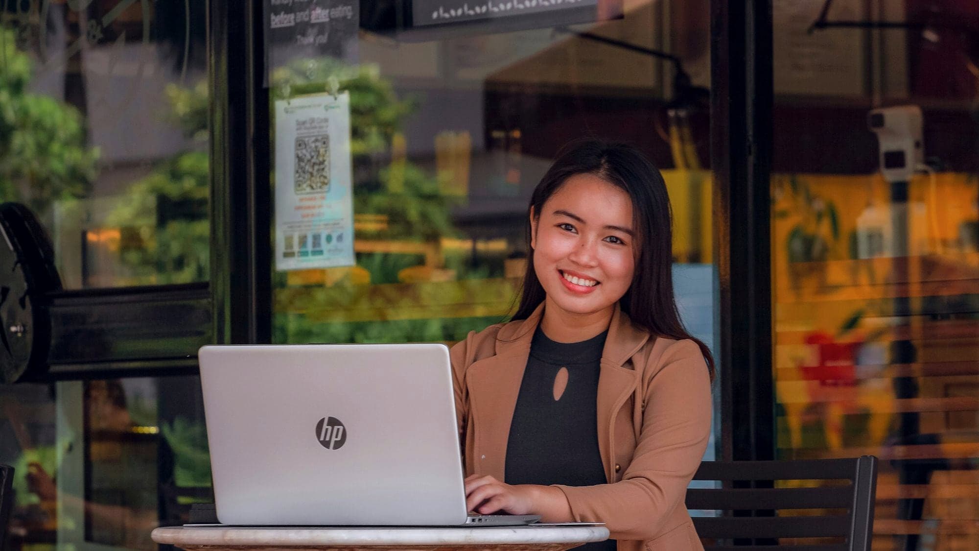 Lächelnde Gründerin arbeitet am Laptop im Eingangsbereich ihres Cafés.